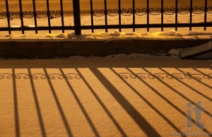 Shadow of fence on snow in orange street light at night. Russia.
