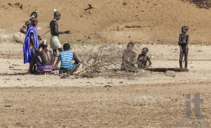 Hamar men teach hunting young boys on a dry river bed.