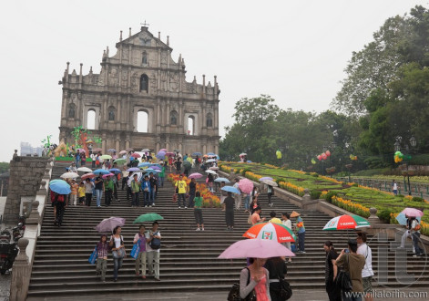 People under colourful umbrellas in front of ruined church of St Paul. Macau. China