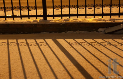 Shadow of fence on snow in orange street light at night. Russia.