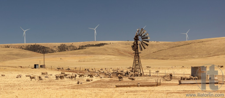 Old broken wind pump and new wind generators distorted by hot air. South Australia.